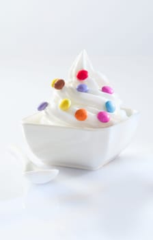Twirled serving of soft-serve icecream covered in colourful round sweets on a white background