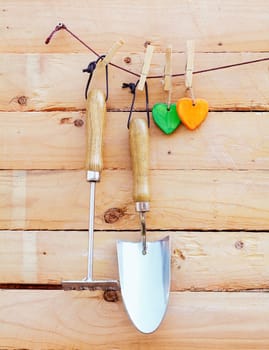 Garden implements hanging on wood with a small trowel and fork or rake alongside two colourful wooden hearts