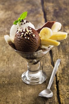 Delicious banana and icecream dessert with sliced fruit served with scoops of chocolate and vanilla icecream on a rustic wooden table