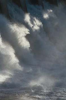 The sun dramatically backlighting the spillway of a large hydroelectric dam overflow.