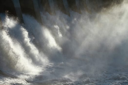 The sun dramatically backlighting the spillway of a large hydroelectric dam overflow.