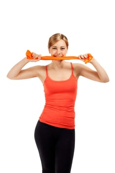Pretty young sportswoman biting into orange fitness band against white background