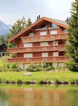 Brown wooden chalet among summer trees and in front of a little lake, Crans Montana, Switzerland