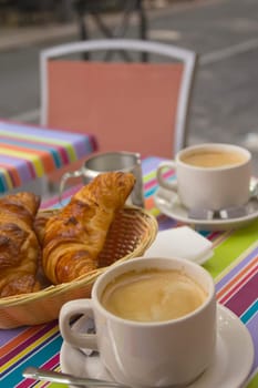 View of the table with two cups of coffee, milk and bread in the basket.