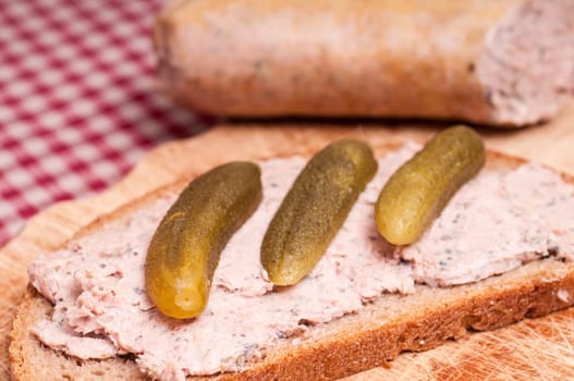 Close-up liver sausage bread with three cucumbers on a wooden board