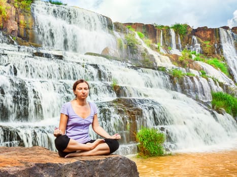 Beautiful woman meditating near waterfall