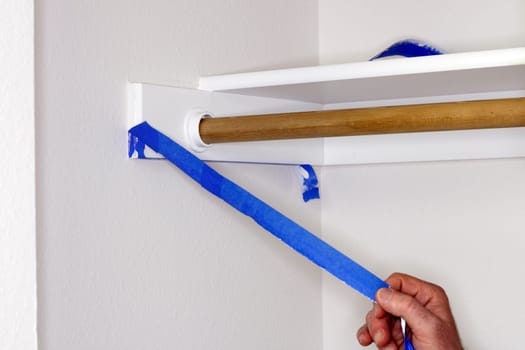 Blue painter&#039 s tape being pulled off of closet shelf bracket after painting the closet walls white.