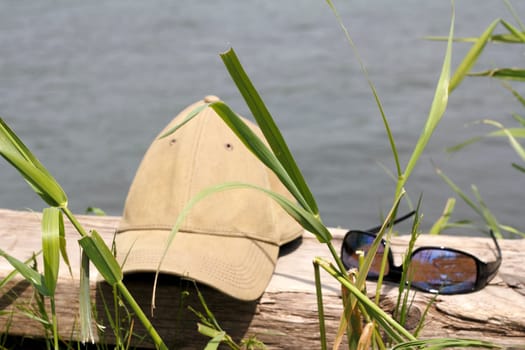 Hat and sunglasses on a wood log with grass in the foreground and Columbia River Gorge river water in the background on a sunny day in Oregon.