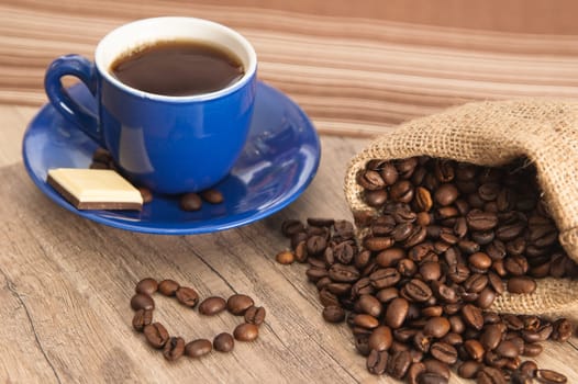Cup of coffee with beans on old wooden surface