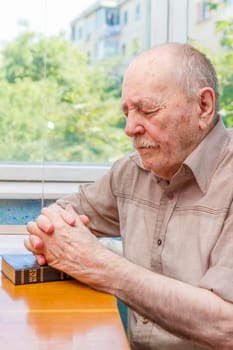 Old man praying at home near the window