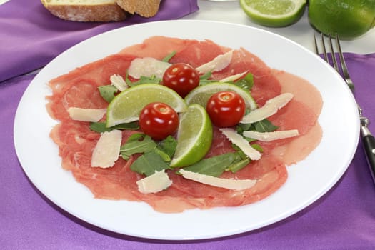 a plate of carpaccio with parmesan,lime and arugula