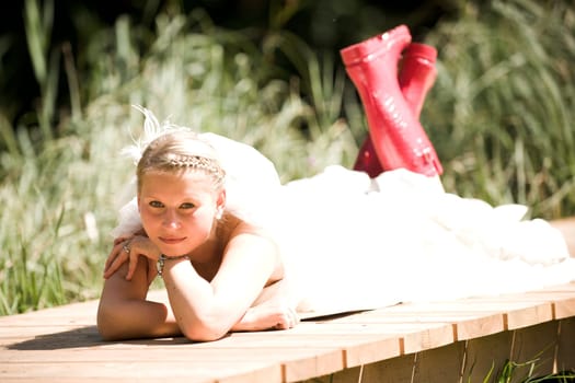 Bride with wedding dress and red rubber boots in nature