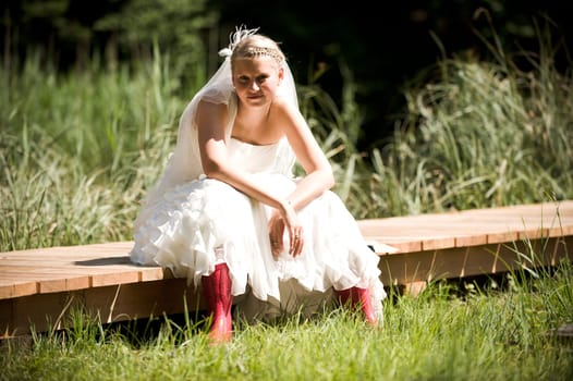 Bride with wedding dress and red rubber boots in nature