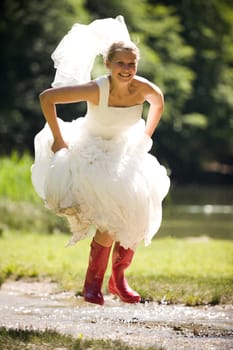 Bride splashes herself wet in small creek with red rubber boots
