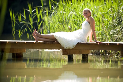 Bride in white wedding dress sitting lonely by a lake