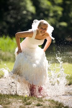 Bride splashes herself wet in small creek with red rubber boots