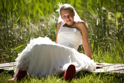Bride with wedding dress and red rubber boots in nature