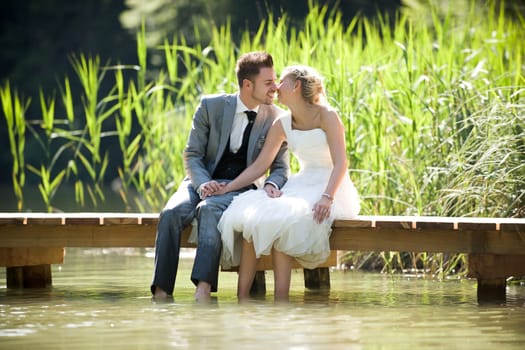 Bride and groom sitting romantically by a lake