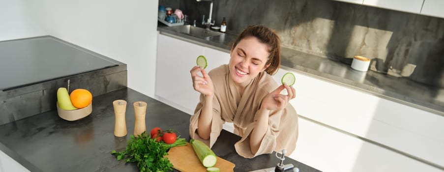 Portrait of beautiful brunette woman in the kitchen, wearing bathrobe, chopping vegetables on board, cooking healthy vegetarian food, preparing salad, making a meal.