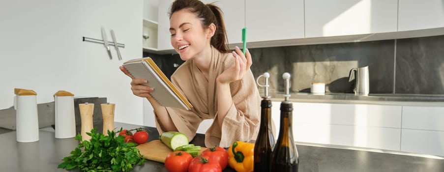 Portrait of modern young woman cooking, making grocery list, reading recipe and making meal, salad in the kitchen, looking at vegetables on chopping board.