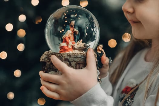 Girl looking at a glass ball with a scene of the nativity of Jesus Christ in a glass ball on a Christmas tree