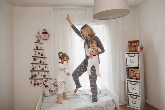 Mother and children in pajamas jumping on the bed in a children room