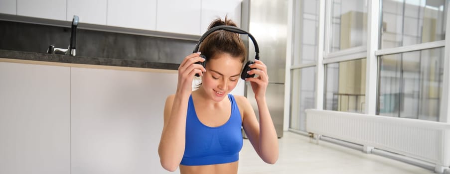 Young woman doing workout training at home, puts on her wireless headphones.