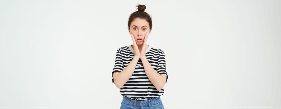 Lifestyle and emotions concept. Portrait of girl with surprised face expression, saying wow, looks impressed at camera, stands over white background.