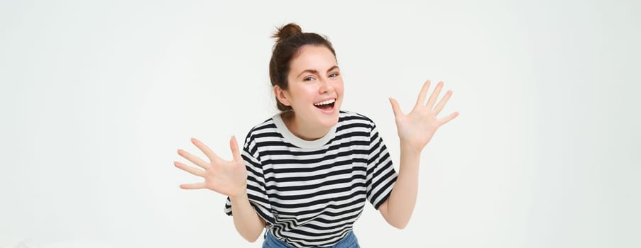 Image of happy, beautiful young woman makes jazz hands, surprise gesture, posing in casual t-shirt and jeans over white background.