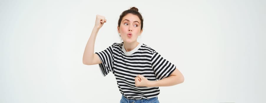 Image of excited young girl cheering, raising hands up, screams from excitement and happiness, winning, celebrating victory, standing over white background.
