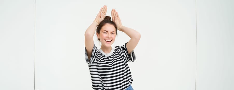 Young woman laughing, showing animal floppy ears gesture with hands on top of head, smiling and looking happy, isolated over white background.