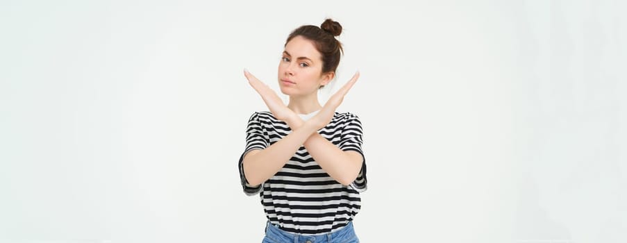 Portrait of confident young woman, showing cross sign, prohibit gesture, disapprove something, isolated against white background.