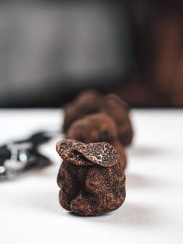 Expensive black truffles gourmet mushrooms on white table in restaurant interior. Row of brown truffles with slice on a white table with dark background. Truffle mushrooms is culinary delight. Close up. Macro.