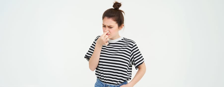 Image of woman digusted by smell, shuts her nose and grimaces, isolated over white background. Copy space