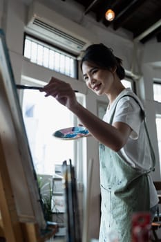 Female artist hold color palette and paintbrush for painting during hobby workshop.