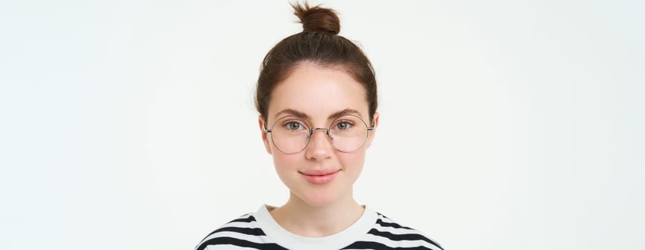 Portrait of beautiful young woman in glasses, wearing eyewear, smiling and looking happy, trying on new spectacles, standing over white background.