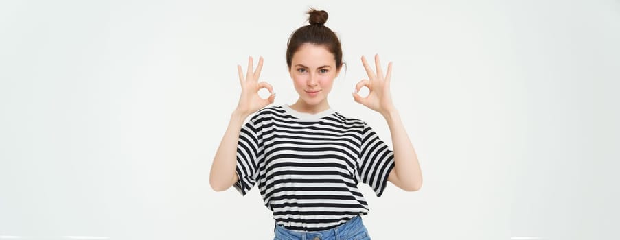 No problem, excellent choice. Smiling, confident young woman, showing okay, ok sign, zero gesture, recommends product, stands over white background.