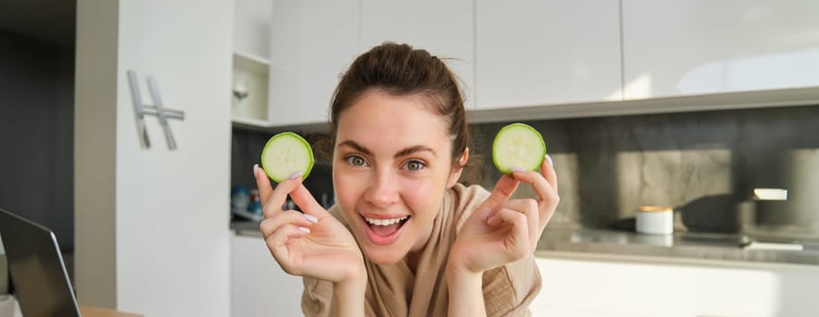 Food and lifestyle concept. Beautiful woman cooking in the kitchen, holding raw zucchini and smiling, preparing healthy vegetarian meal, making salad, looking happy.