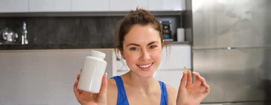 Close up portrait of beautiful, smiling fitness woman, showing vitamin, bottle with dietary supplement for better workout result, healthy and strong body.