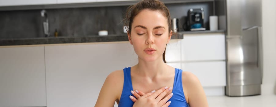 Woman practicing yoga and meditation at home sitting in lotus pose on yoga mat, relaxed with closed eyes. Mindful meditation concept. Wellbeing.