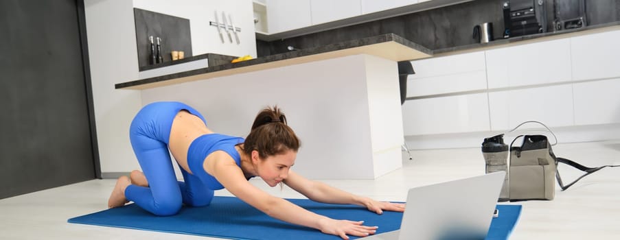 Image of young sportswoman, fitness girl watching online yoga tutorial on laptop and exercising, following video instructions.