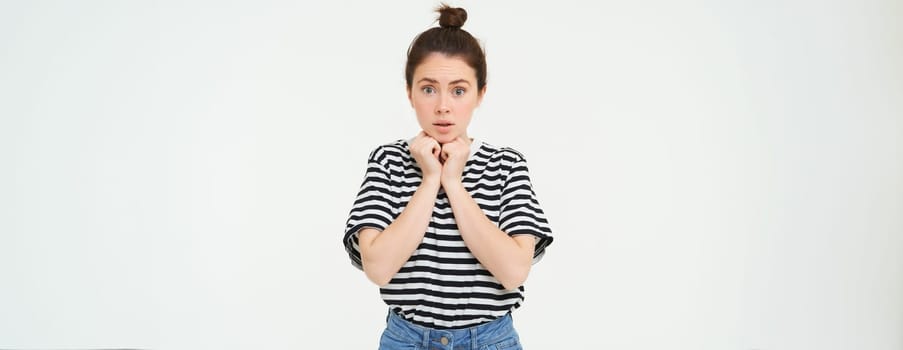 Portrait of young compassionate woman, looking with sympaty, gasping at camera, raising eyebrows, standing over white background.