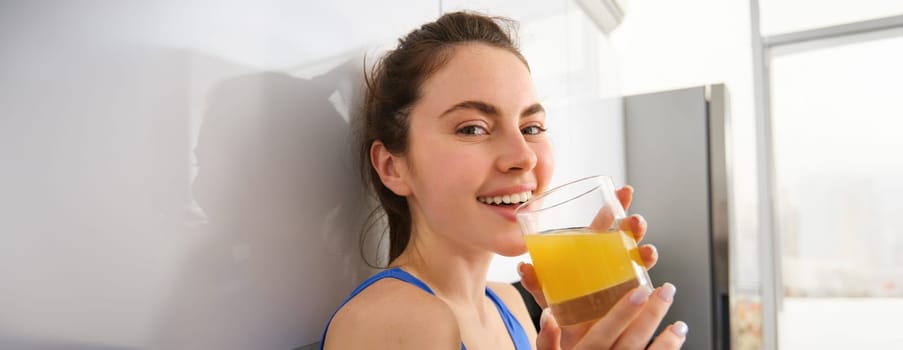 Portrait of smiling brunette sportswoman, drinking fresh juice, detox drink, enjoys freshly squeezed beverage after workout training session.