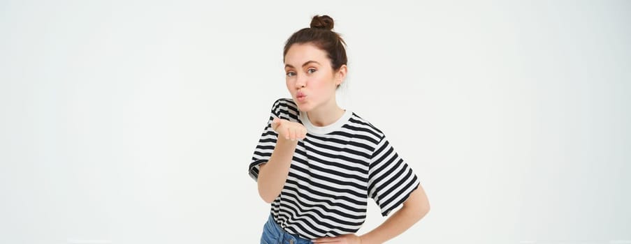 Portrait of cute young woman blows air kiss, sends mwah at camera, posing cute against white background. Lifestyle and people concept.