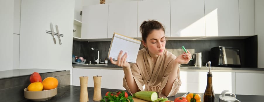 Portrait of modern young woman cooking, making grocery list, reading recipe and making meal, salad in the kitchen, looking at vegetables on chopping board.