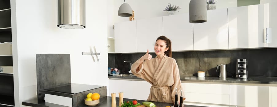 Portrait of beautiful young woman in her home clothes, chopping vegetables, holding knife and cutting zucchini, cooking in kitchen, preparing food for family dinner.