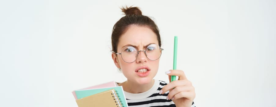 Portrait of angry woman in glasses, teacher scolding someone, shaking pen and arguing, holding notebooks, standing over white background.