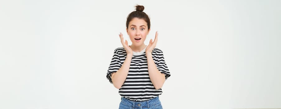 Portrait of surprised woman gasping, looking amazed, hear great news, drops jaw, says wow, impressed by something, stands over white background.