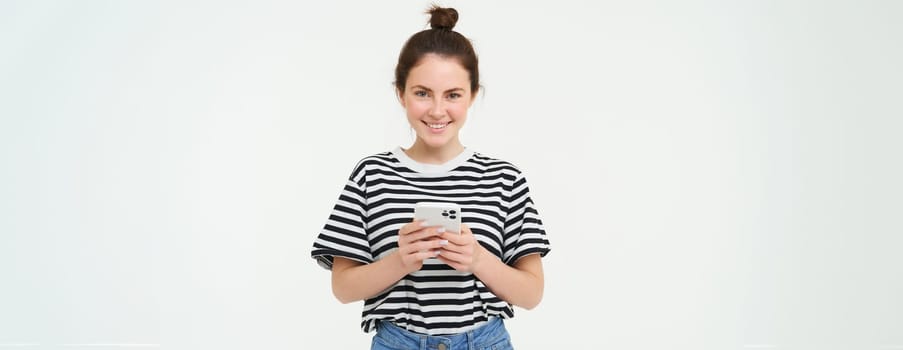 Technology and people concept. Young woman with mobile phone, smiling, using smartphone app, social media application, isolated over white background.
