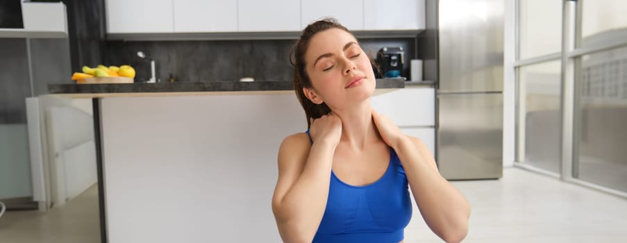 Image of woman workout at home, stretching her head and neck, does warm-up exercises before yoga, fitness training in living room.